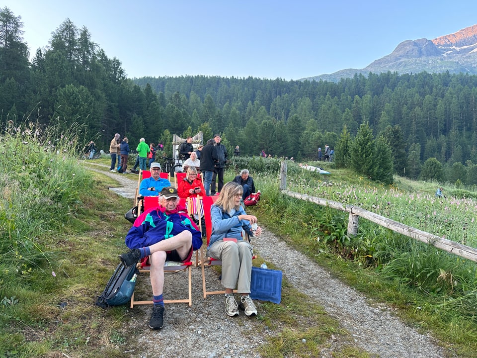 Menschen sitzen auf Liegestühlen auf einem Wanderweg in den Bergen.