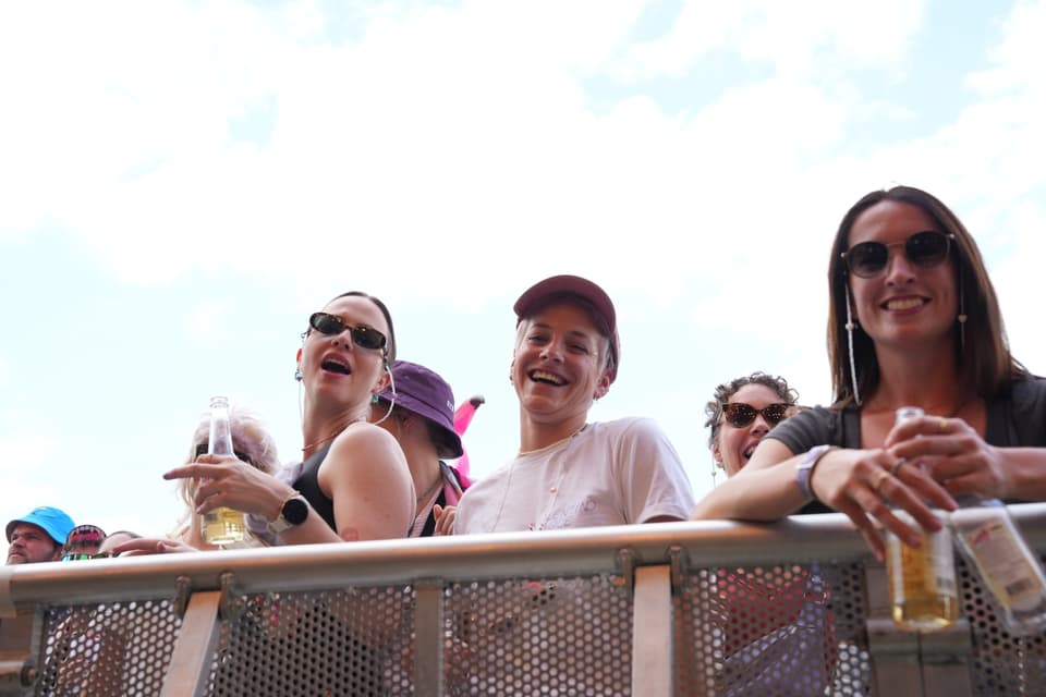 Mehrere Menschen stehen hinter einer Absperrung und lächeln am Open Air Lumnezia 2024.