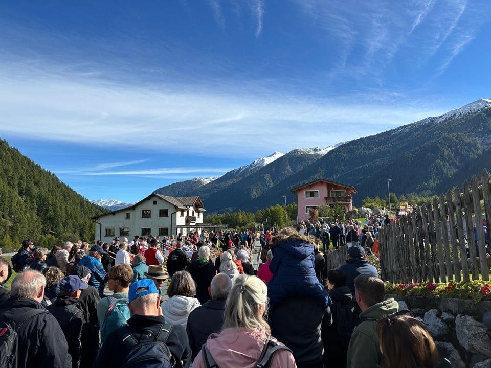 Menschenmenge vor Häusern in bergiger Landschaft.