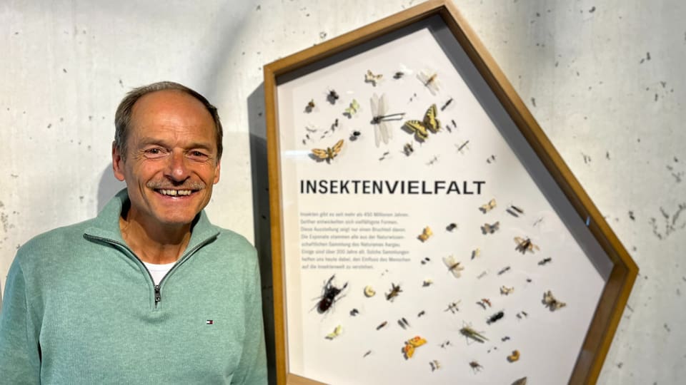 Hans Lozza neben Ausstellungsschild mit Insekten.