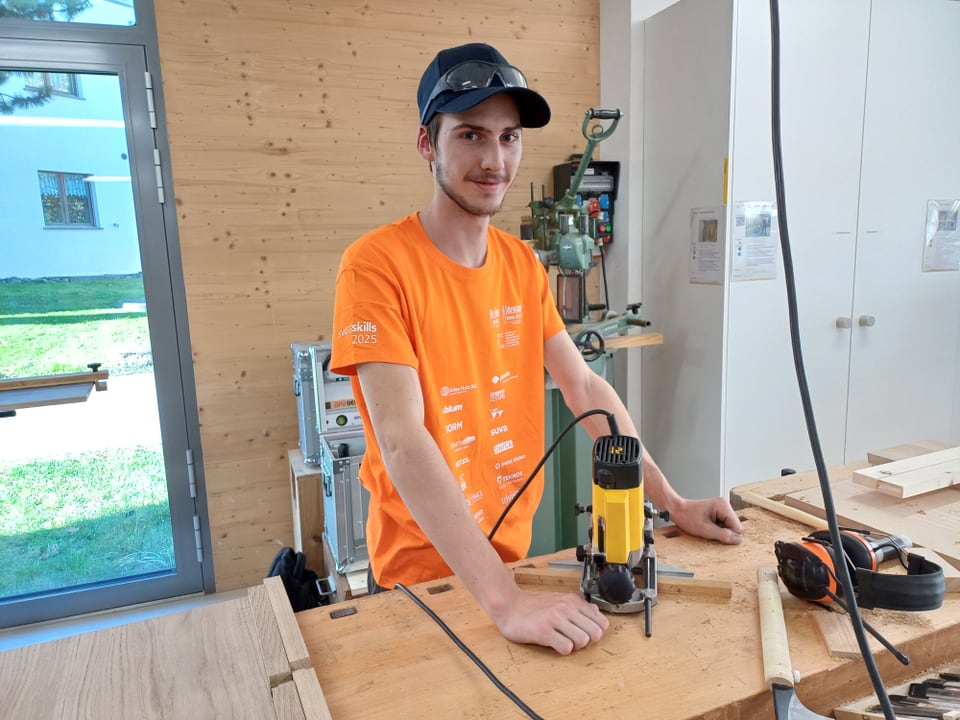 Mann in orangefarbenem T-Shirt arbeitet mit einer Oberfräse in Werkstatt.