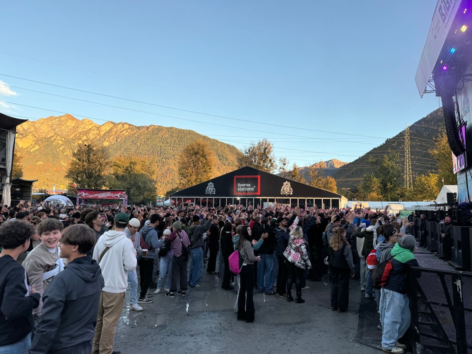 Menschenmenge bei einem Outdoor-Konzert vor Bergkulisse.