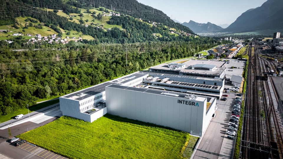 Luftbild einer grossen Fabrikanlage mit umliegender Landschaft und Bergen.