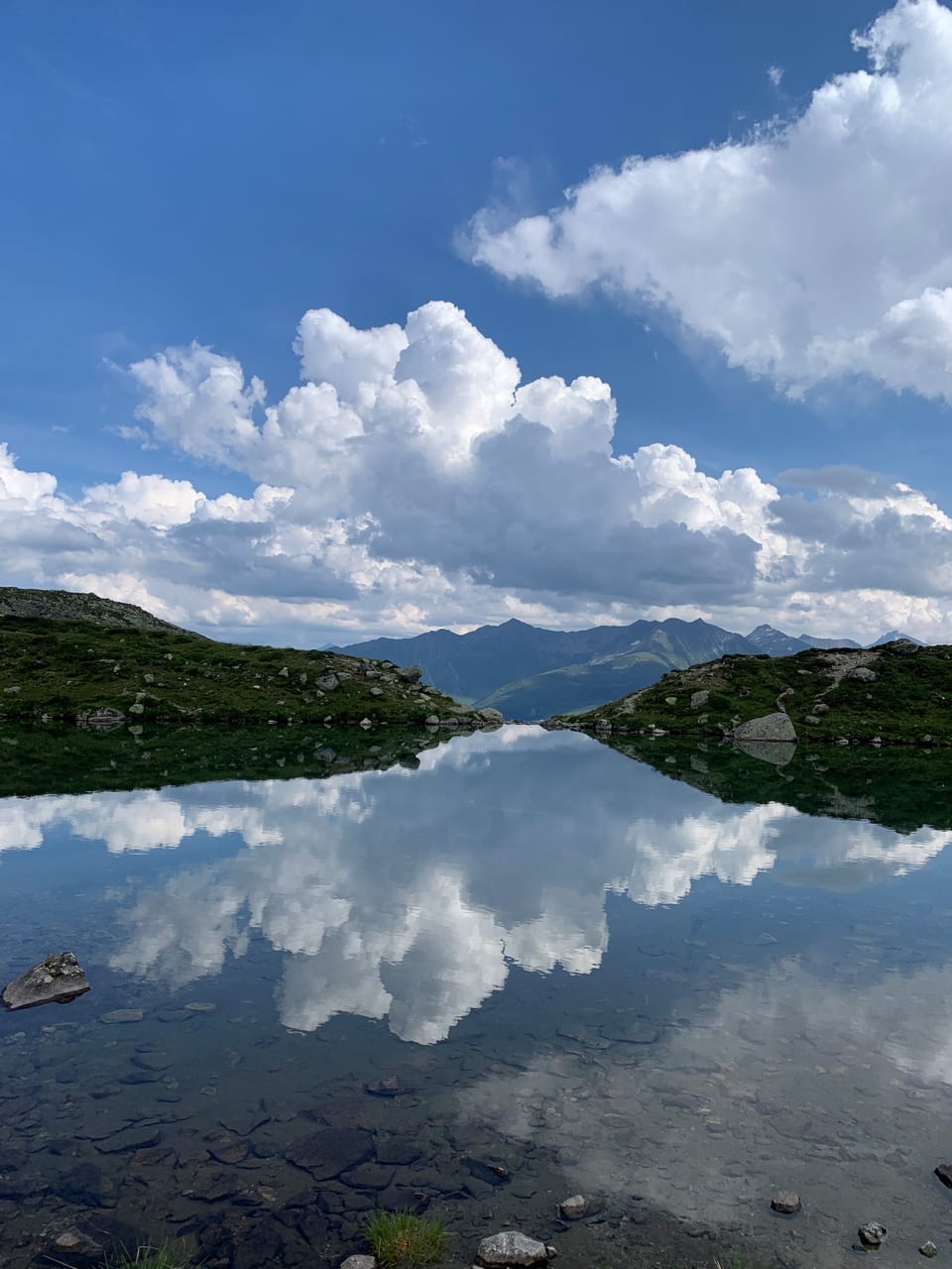 Wolken spiegeln sich in einem klaren Bergsee.