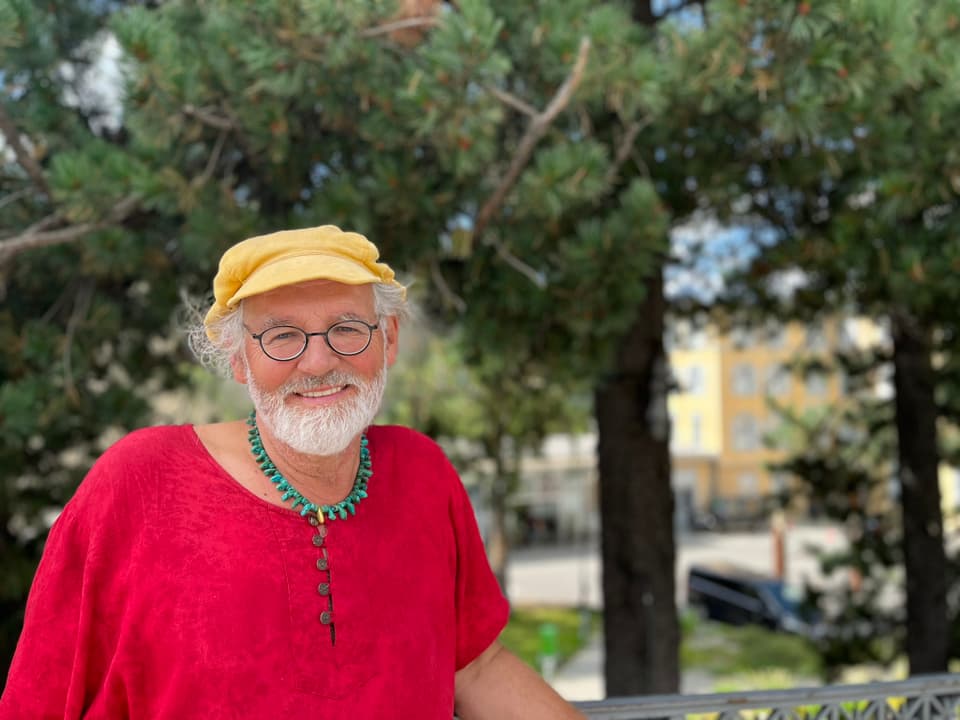 Mann mit rotem Hemd und gelbem Hut vor Bäumen.