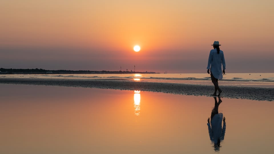 Person bei Sonnenuntergang am Strand spazierend.