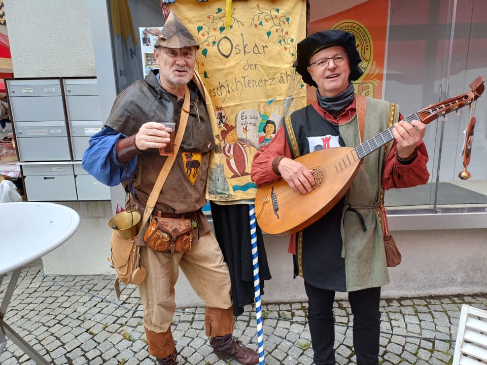 Zwei Männer in mittelalterlicher Kleidung, einer mit Getränk, einer mit Laute.