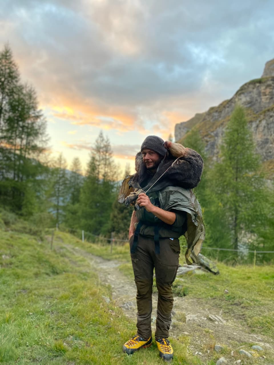 Wanderer auf Bergweg mit Abendhimmel im Hintergrund.