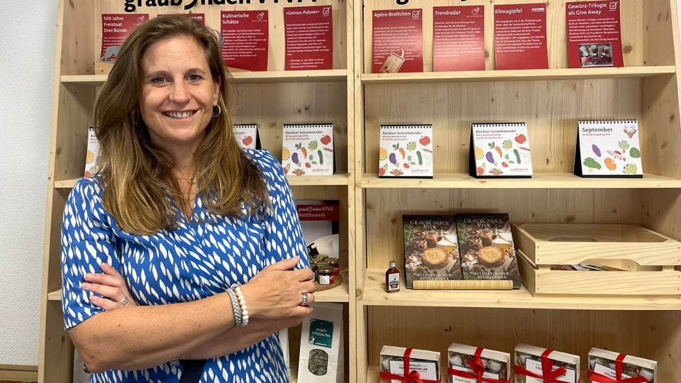 Frau in blauem Hemd vor Holzregalen mit Produkten.