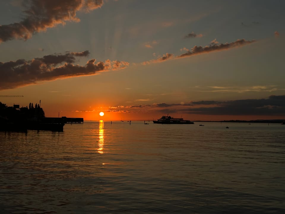 Sonnenuntergang über einem See mit Schiff und Wolken am Himmel.