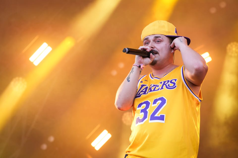 Mann in gelbem Lakers-Trikot performt auf Bühne EAZ am Open Air Lumnezia 2024..