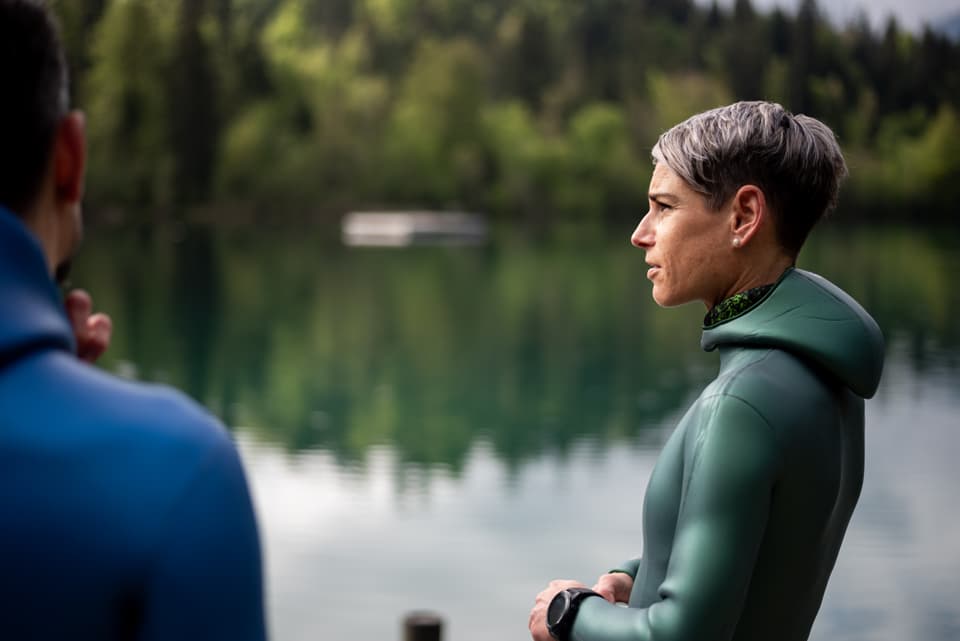 Frau im Neoprenanzug steht an einem See.