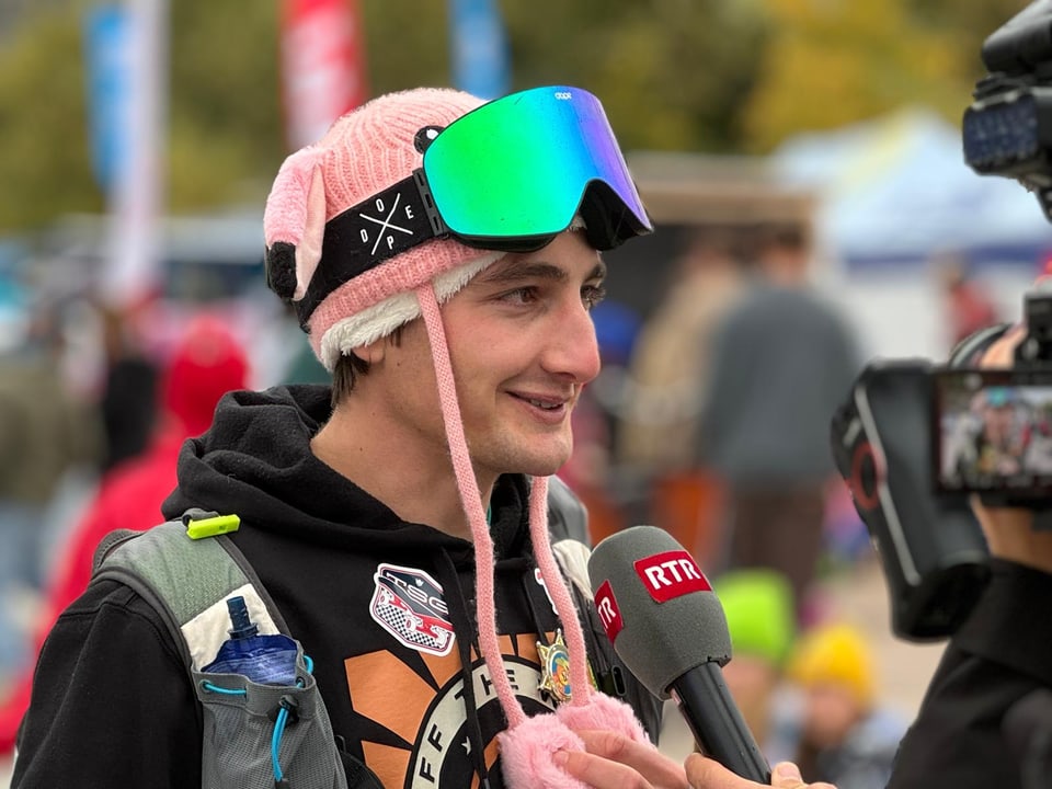 Big Air Chur 2024: Person im Gespräch mit TV-Journalist, Mikrofon, trägt bunte Skibrille und pinke Mütze.