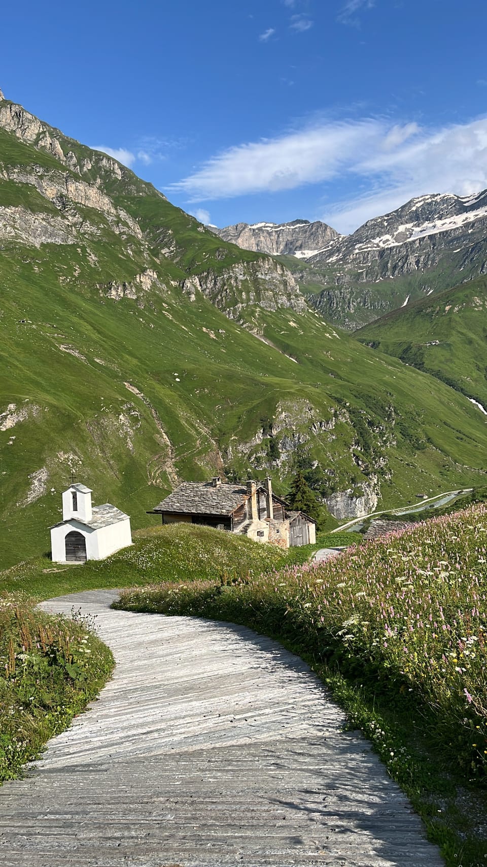 Gebirgspfad, der zu einer kleinen Kirche und einem Haus in den Alpen führt.