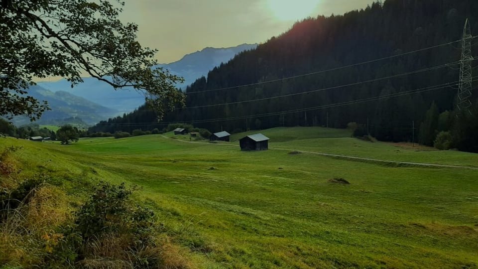 Grüne Wiese mit Hütten in den Bergen bei Sonnenuntergang.