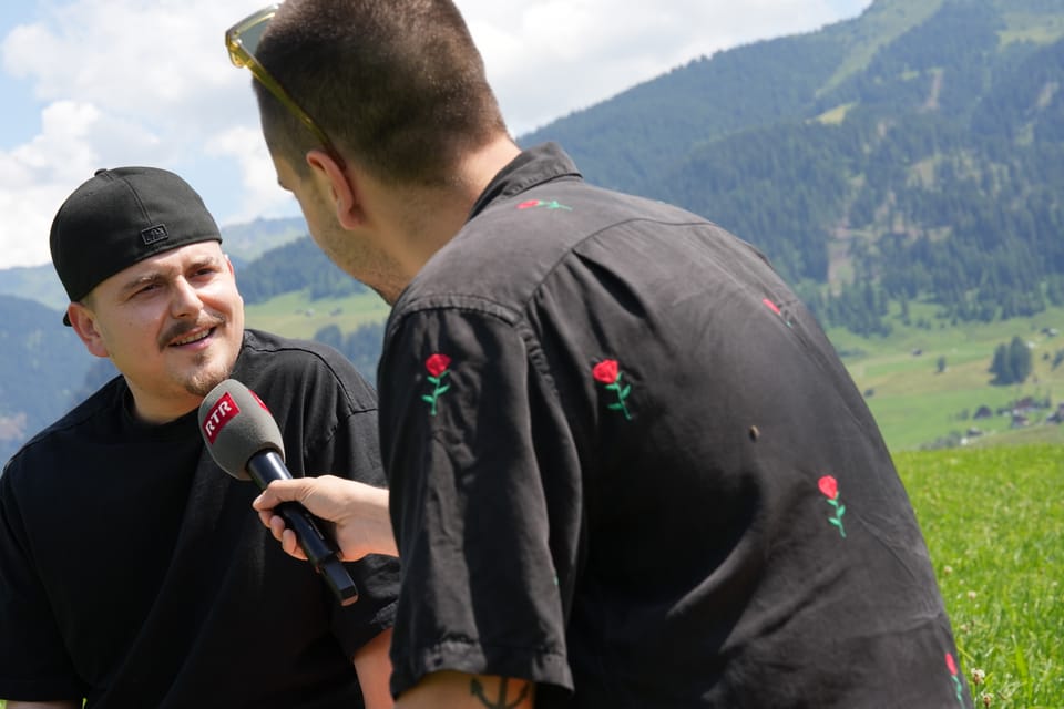 Interview im Freien mit Mikrofon vor Berglandschaft Elias Tsoutsaios im INterview mit EAZ am Open Air Lumnezia 2024.
