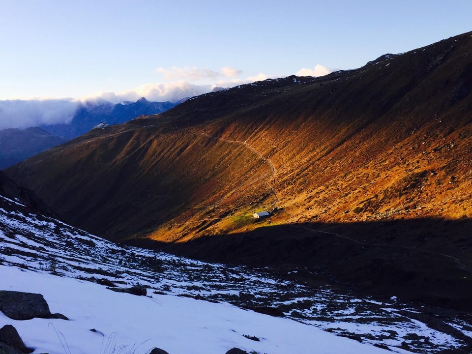 Gebirgstal im Sonnenuntergang mit Schneeflecken.