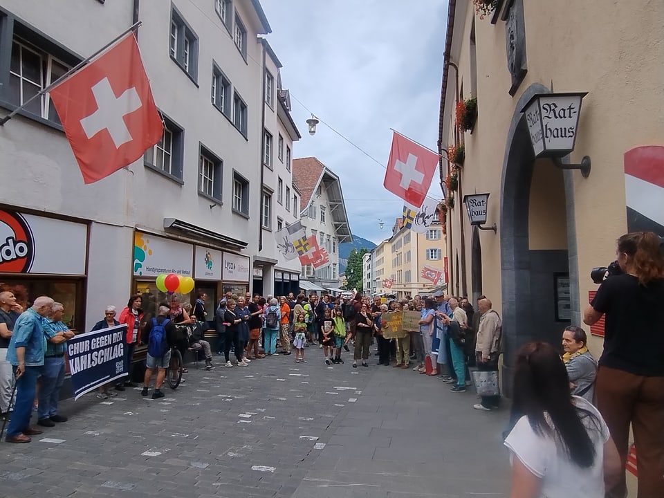 Strassenszene mit schweizer Flaggen und Menschenmengen vor dem Rathaus.