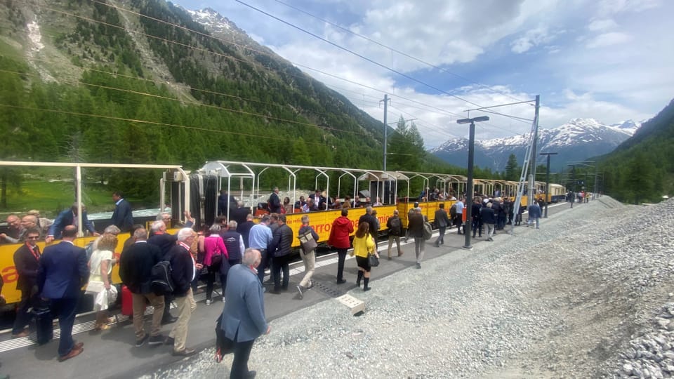 Menschen steigen an einem Bergbahnhof in einen gelben Zug ein.