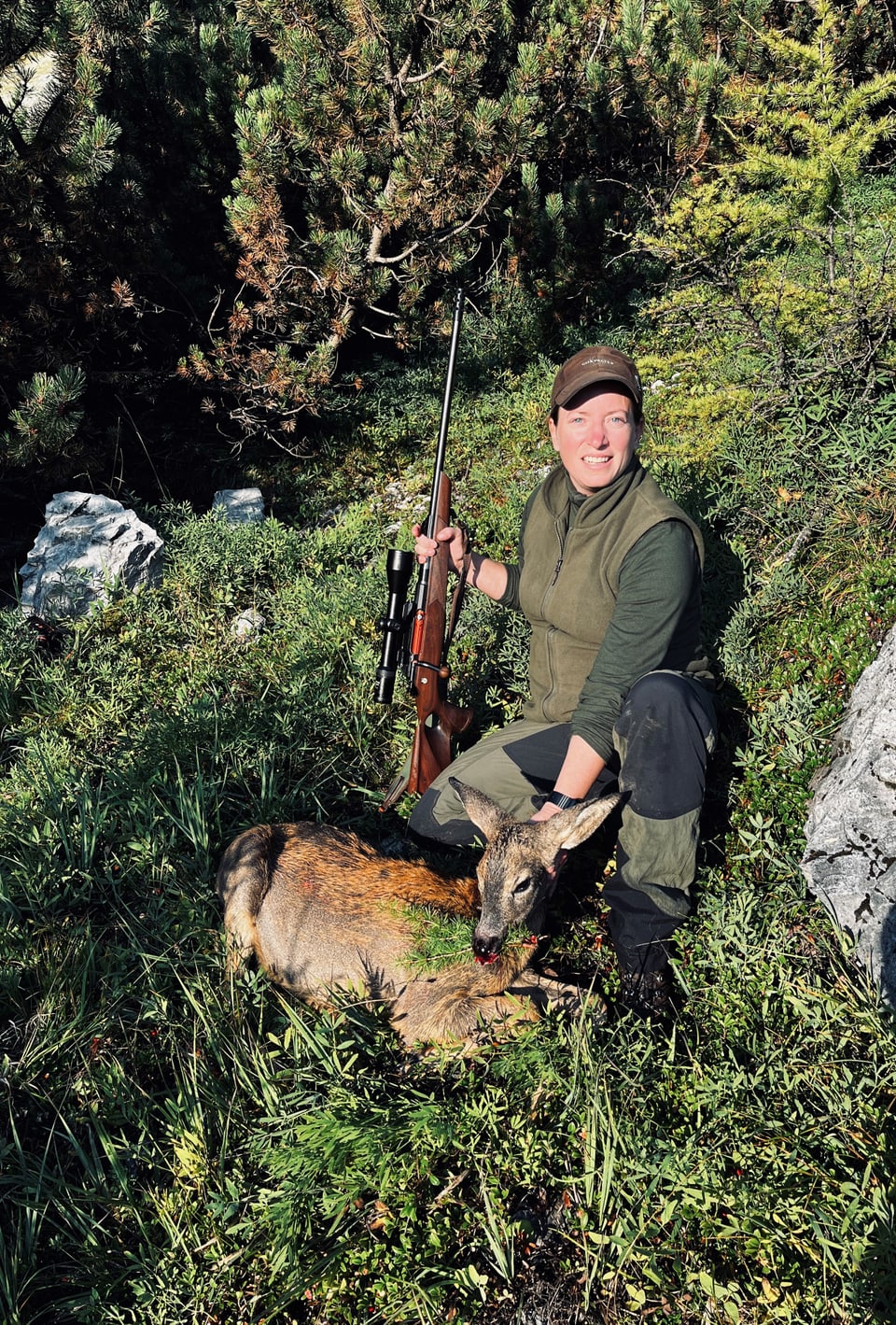 Jägerin mit Gewehr und erlegtem Hirsch im Wald.