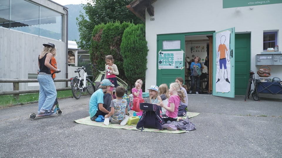 Die Kinder sitzen im Kreis vor dem Schulzimmer.